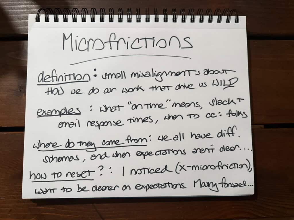 A handwritten note on a spiral-bound notepad titled “Micro-frictions.” It defines micro-frictions as small misalignments in how work is done that cause frustration. Examples listed include differing interpretations of “on time,” expectations for Slack or email response times, and when to CC others. The note explains these issues arise from different personal schemas and unclear expectations, and suggests resolving them by naming the micro-friction and clarifying expectations moving forward.