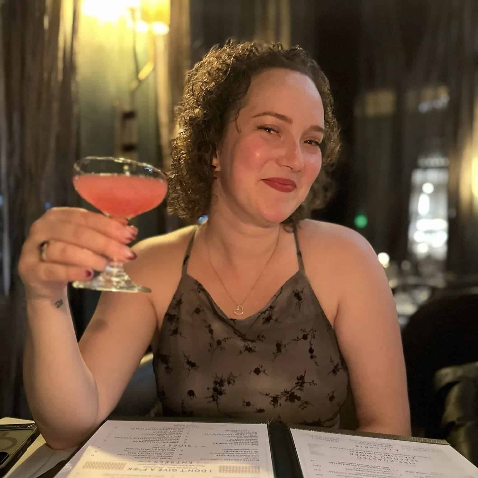 Sophia Zisook raising a pink cocktail and smiling at a restaurant.