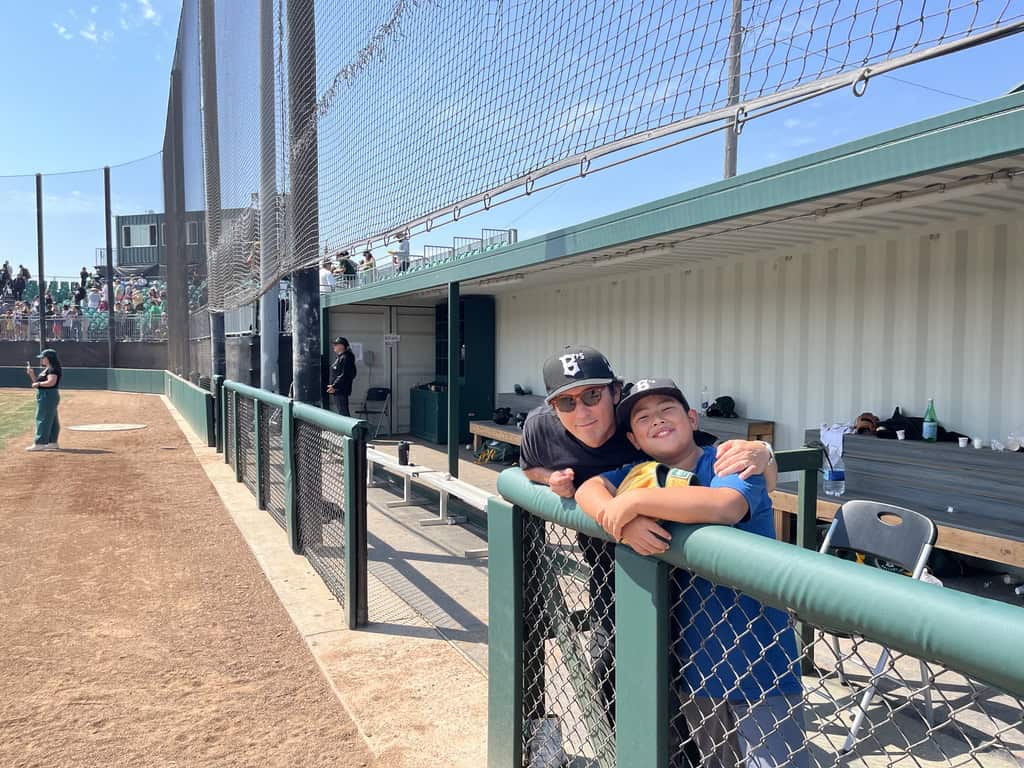 A man and his son pose in a dugout at a baseball game.