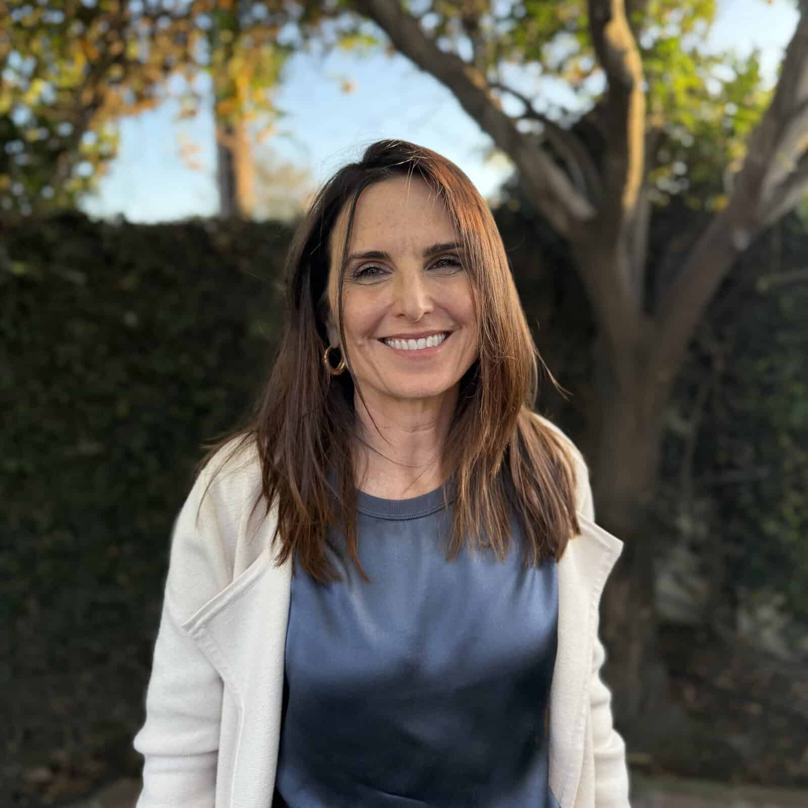 A woman smiles in the outdoors near a tree