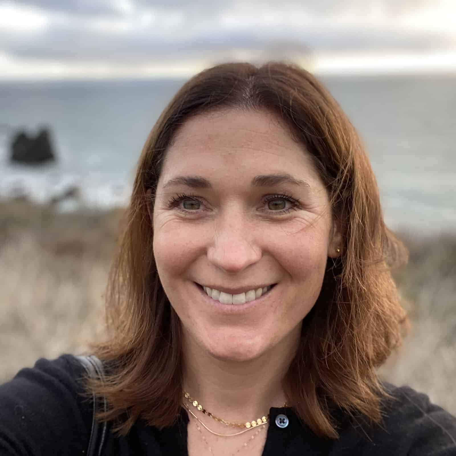 Woman smiles with beach in background.
