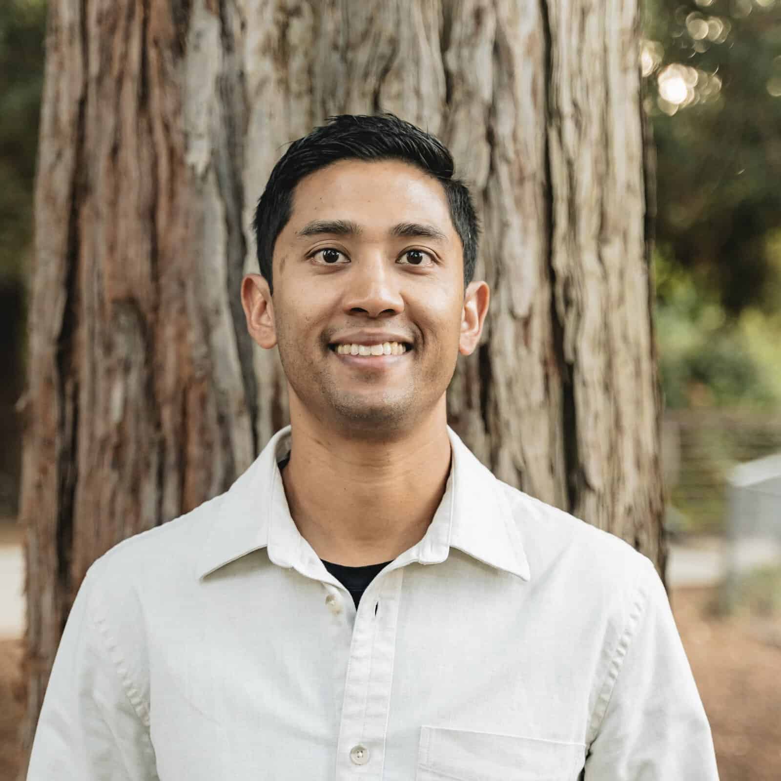 a man smiles by a tree