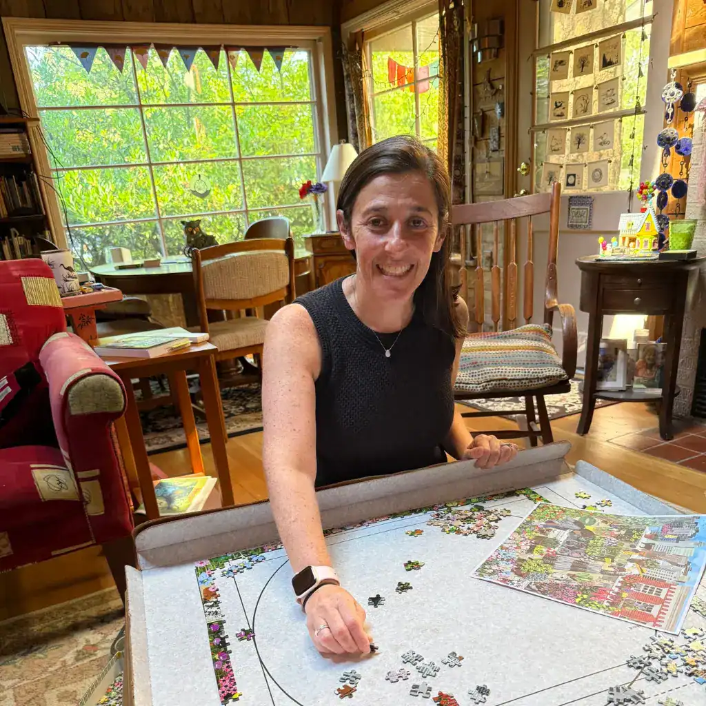 A woman enjoys a quiet moment of mindfulness while assembling a detailed jigsaw puzzle in a warm, bright home environment.