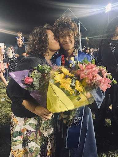 High school graduation, both holding large bouquets of flowers, with other graduates visible in the background.