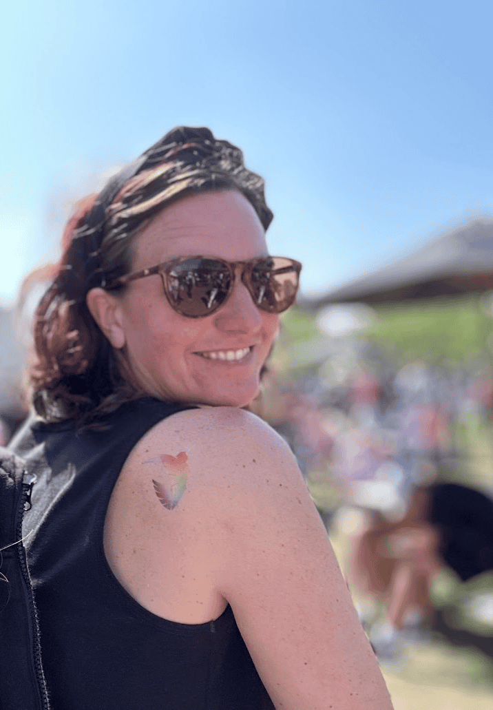 Woman wearing sunglasses smiling over her shoulder outdoors on a sunny day.
